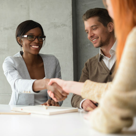 Two women and a man in a meeting with the two women shaking hands