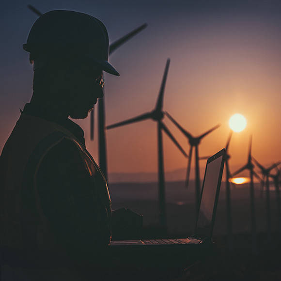 Construction worker using laptop with wind farm in background at sunset